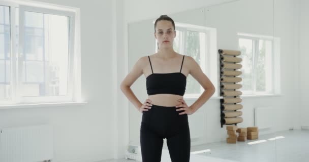Chica europea en ropa deportiva mira a la cámara, sus manos en la cintura — Vídeos de Stock