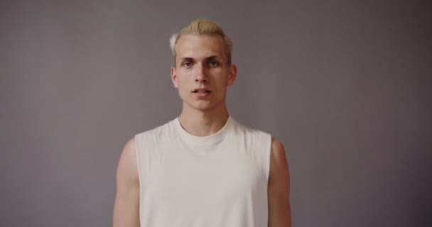 Blond ung man tittar allvarligt på kameran, lutar huvudet åt sidan — Stockvideo