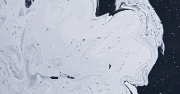 Vopseaua albă curge în sclipici negre, culori abstracte se rotesc și explodează . — Videoclip de stoc