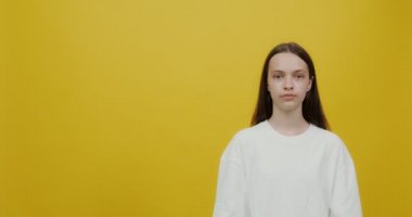 Genç bir kadın, elleri neşe ve gülümsemeyle boş bir arkaplan gösterir.