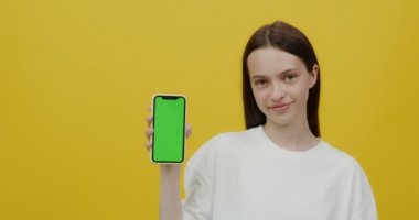 Avrupalı görünümlü genç bir kadın gülümsüyor, elinde bir telefon tutuyor.
