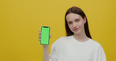 Avrupalı görünümlü genç bir kadın gülümsüyor, elinde bir telefon tutuyor.