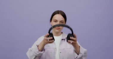 Avrupalı genç bir kadın kameraya ciddi ciddi bakar ve kulaklık takar.