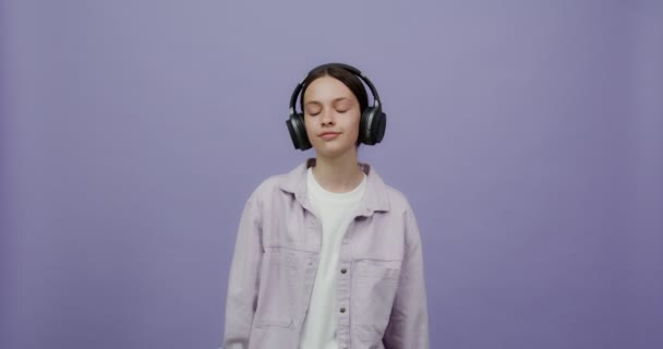 Eine ernsthafte junge Frau setzt Kopfhörer auf und beginnt zu tanzen und zu lächeln — Stockvideo