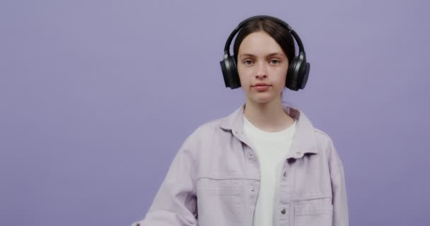 Una joven con auriculares sostiene un móvil en la mano con la pantalla hacia adelante — Vídeos de Stock