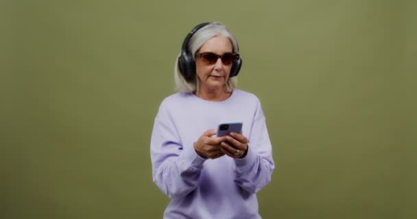 Uma mulher adulta usando fones de ouvido dança e mastiga chiclete — Vídeo de Stock