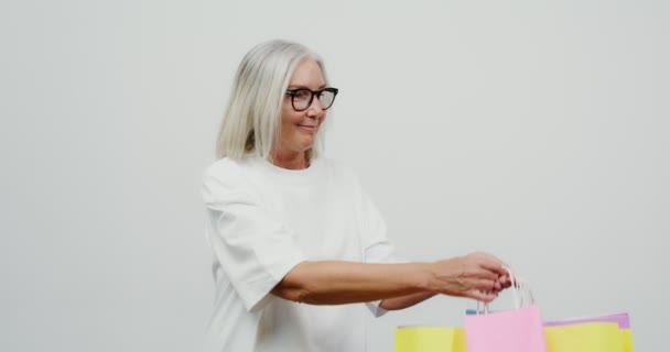 Mujer adulta de pelo gris jugando con bolsas de papel multicolores en sus manos — Vídeo de stock