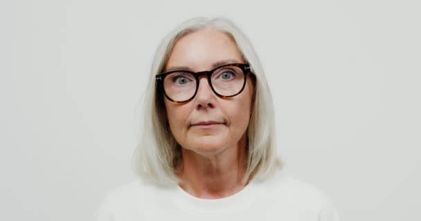 Una mujer adulta de pelo gris con gafas mira seriamente a la cámara — Vídeo de stock