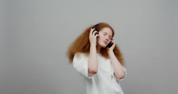 Ένα κοκκινομάλλικο κορίτσι με πλούσια μαλλιά βάζει ακουστικά και αρχίζει να χορεύει — Αρχείο Βίντεο