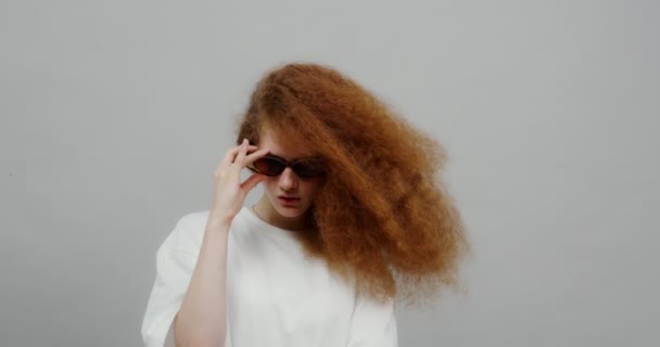 Egy gyönyörű vörös hajú lány, buja hajjal, napszemüveget vesz fel. — Stock videók