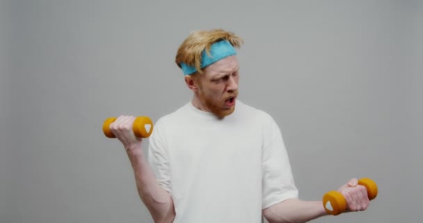 A red-haired guy pretends that it is difficult for him to lift small dumbbells — Stock Video