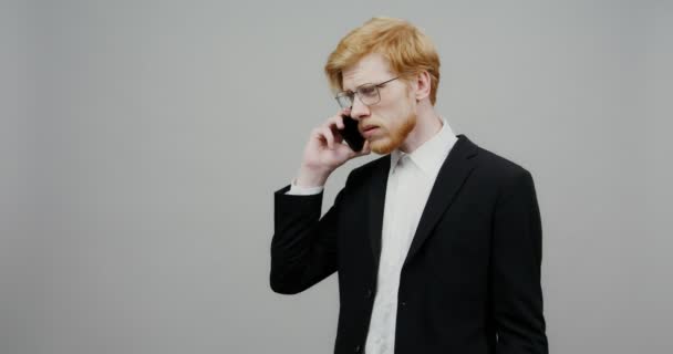 Un tipo serio vestido con un traje de negocios, está hablando en un teléfono móvil — Vídeos de Stock