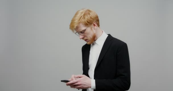 Un tipo serio vestido con un traje de negocios, está enviando mensajes de texto en un teléfono móvil. — Vídeo de stock