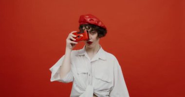 Esmer bir kadın kırmızı bir kamerada fotoğraf çekiyor ve gülüyor.