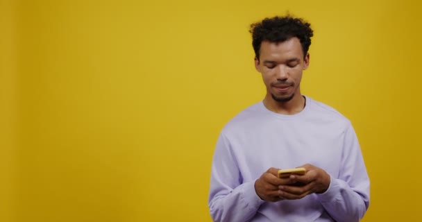 Un joven mulato está enviando mensajes de texto en un teléfono móvil y sonriendo — Vídeos de Stock