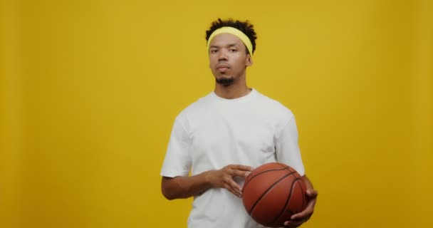 A young mulatto man looks seriously into camera, throwing a basketball — Stock Video