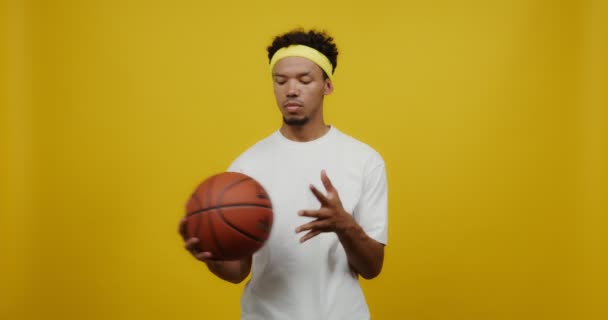 Un joven mulato mira seriamente a la cámara, lanzando una pelota de baloncesto — Vídeo de stock