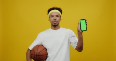 Basketbol oynayan genç melez adam ve önünde ekranı olan mobil.