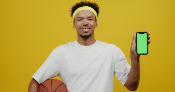 Joven mulato hombre celebración de baloncesto y móvil con pantalla hacia adelante — Vídeos de Stock