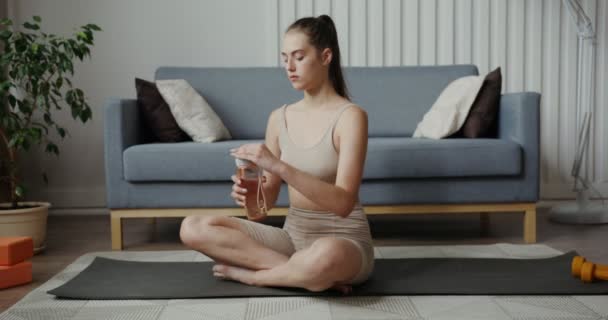 Fille européenne en vêtements de sport boit de l'eau de la bouteille, assis en position lotus — Video
