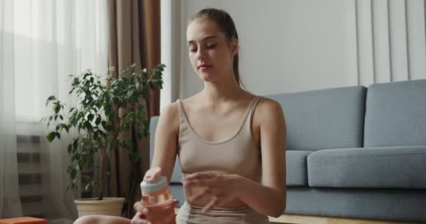 Európai lány sportruházat iszik vizet palack, ül lótuszpozícióban — Stock videók