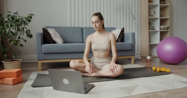 Chica europea en ropa deportiva utiliza un ordenador portátil sentado en posición de loto — Vídeo de stock