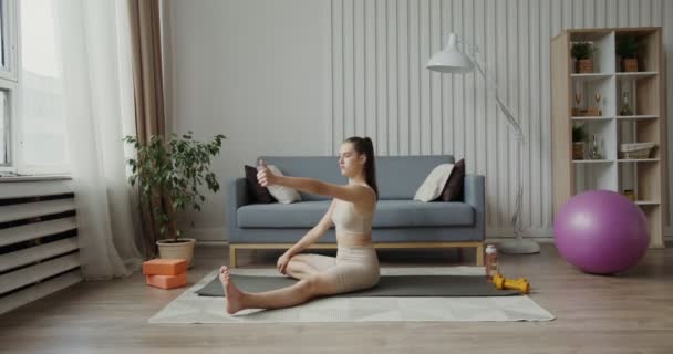 Fille européenne vêtue de vêtements de sport, faire des exercices assis sur un tapis de gymnastique — Video