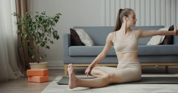 Chica europea vestida con ropa deportiva, haciendo ejercicios sentados en una alfombra de gimnasia — Vídeos de Stock