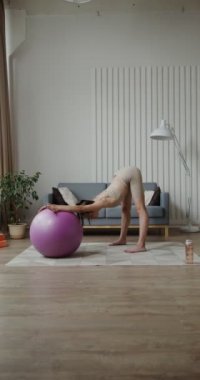 Spor kıyafetleri giymiş Avrupalı bir kız topla esneme egzersizleri yapıyor.