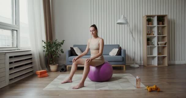 European girl dressed in sportswear smiling at camera sitting on gymnastic ball — Stock Video