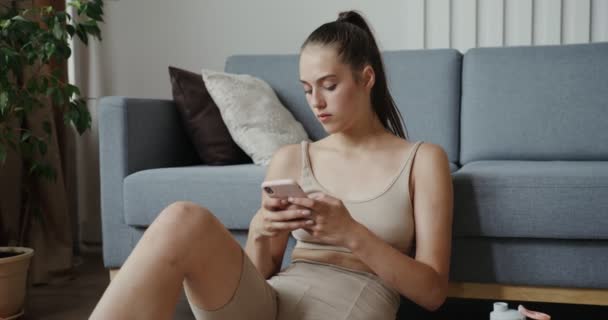 Chica europea vestida con ropa deportiva sentada en el suelo usando el teléfono — Vídeos de Stock