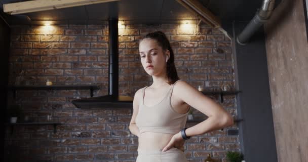 Европейская девушка в спортивной одежде смотрит в камеру с руками на поясе — стоковое видео