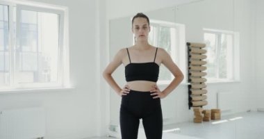 Spor giyinen Avrupalı bir kız elleri belinde kameraya bakıyor.