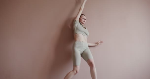 Europeisk flicka i sportkläder som gör gymnastik nära väggen — Stockvideo