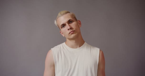 Blonder junger Mann blickt ernst in die Kamera und neigt seinen Kopf zur Seite — Stockvideo