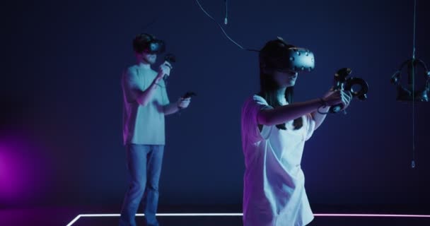 Bir adam ve bir kadın ellerinde joysticklerle sanal gerçeklik gözlüğü takıyor. — Stok video