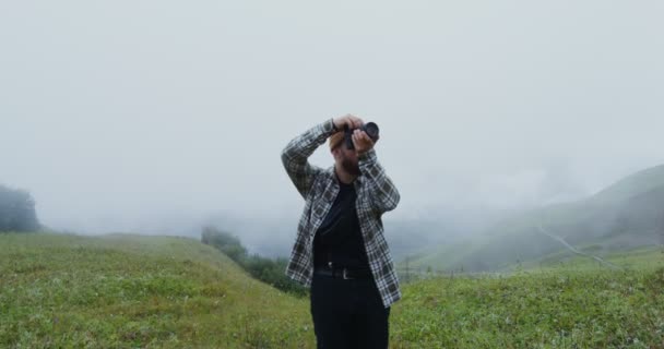 Россия, Кавказ. Молодой человек фотографирует стоя на травянистом склоне холма — стоковое видео