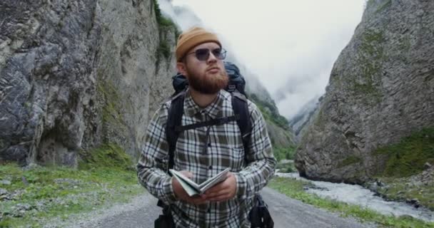 Kaukasus. Ein junger Mann studiert Landkarte, während er auf breiter Straße zwischen den Felsen steht — Stockvideo