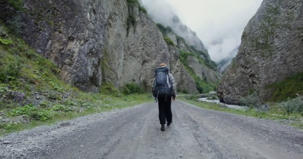 Rusko, Kavkaz, Elbrus. Turista kráčí po široké cestě mezi skalami — Stock video