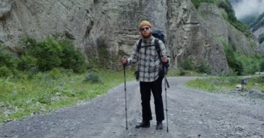 Genç bir adam elinde sopalarla kayaların arasında yürüyor. Kafkaslar.