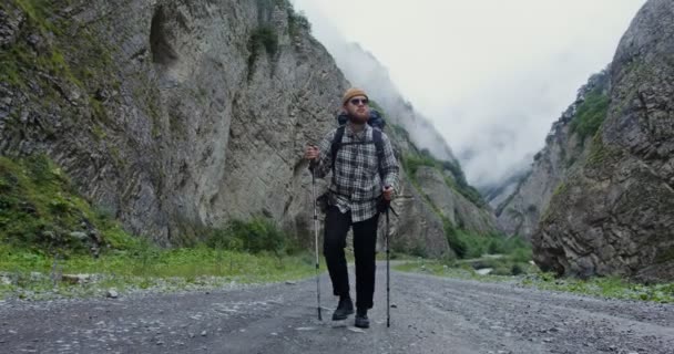 Een jongeman loopt met stokken voor sport wandelen tussen de rotsen. De Kaukasus — Stockvideo