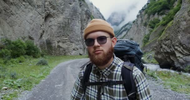 De Kaukasus. Een jongeman staat op de weg tussen de rotsen en glimlacht — Stockvideo