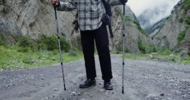 Genç bir adam elinde sopalarla kayaların arasında yürüyor. Kafkaslar.