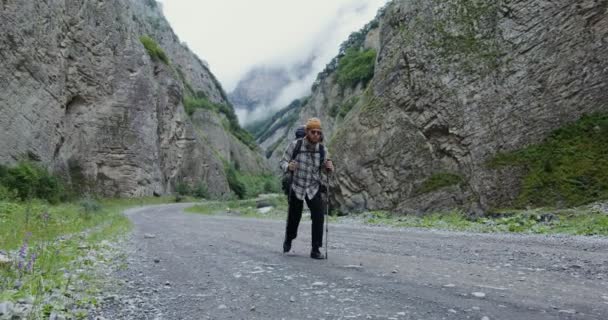 Um jovem caminha com paus para esportes andando entre as rochas. O Cáucaso — Vídeo de Stock