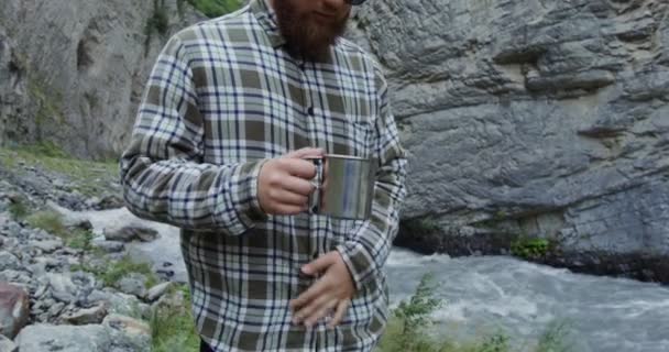 Russia, Caucaso. Giovane uomo beve da una tazza, in piedi vicino a un fiume di montagna — Video Stock
