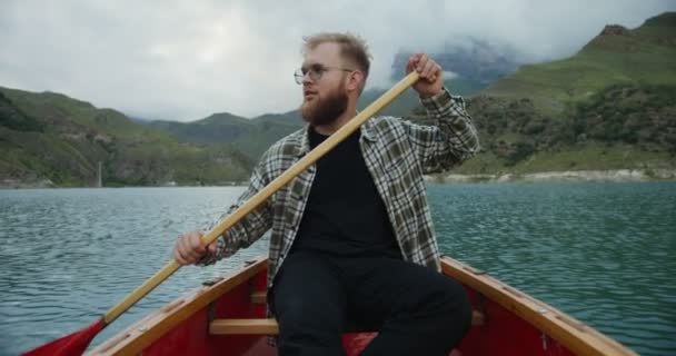 Russland, Kaukasus. Ein junger Mann segelt mit einem Ruderboot auf einem See zwischen den Bergen — Stockvideo