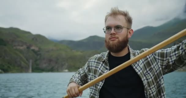 Russia, Caucaso. Un giovane sta navigando in barca a remi sul lago tra le montagne — Video Stock