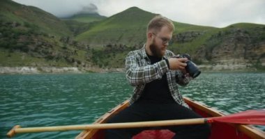 Rusya, Kafkasya. Bir adam teknede, dağların arasında resim çekiyor.