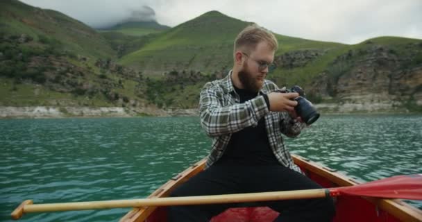 Russland, Kaukasus. Ein Mann fotografiert auf einem Boot, auf einem See zwischen Bergen — Stockvideo