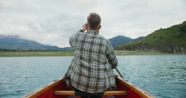 ロシア、コーカサス。若い男が山の間の湖でボートに乗って航海している — ストック動画